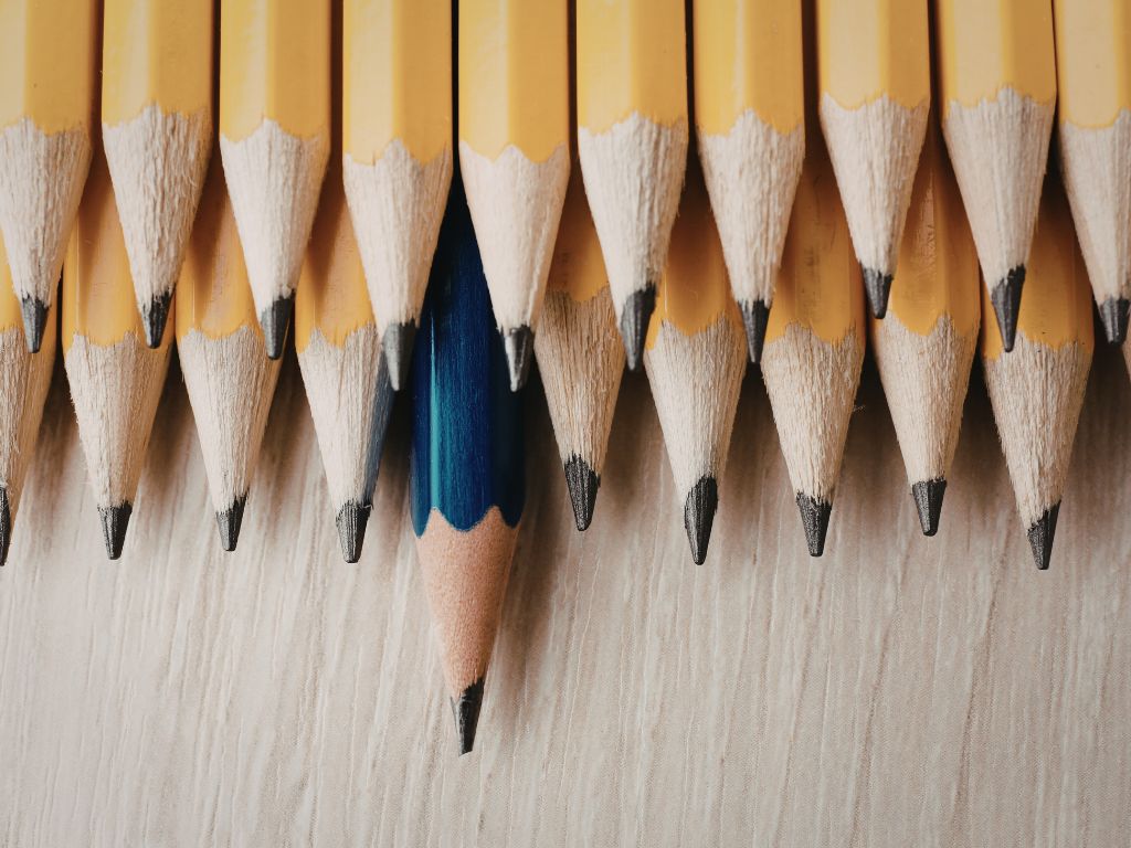 Niebieski ołówek wyróżniający się z grupy żółtych, symbolizujący indywidualność i kreatywność w erze copywritingiem z AI.